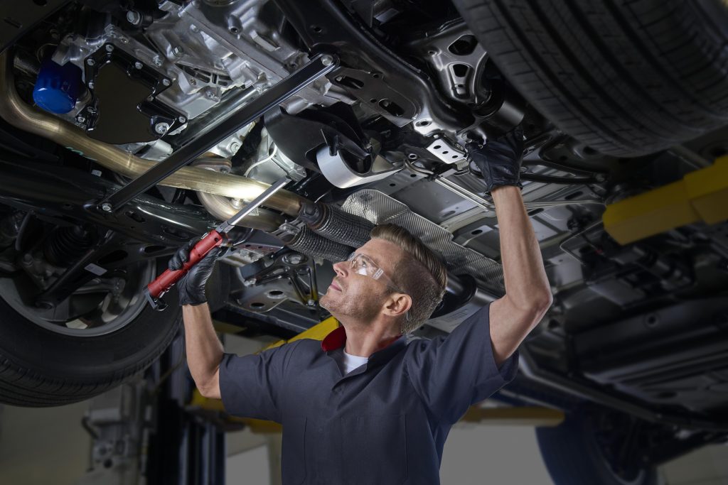 Mechanic inspecting vehicle undercarriage on lift.